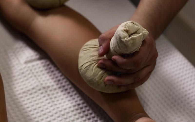Masseur doing spa massage of leg with herbal compresses bag Thai method. Close up of relaxing massage for woman at spa salon, wellness herbal massaging leg. Relax massage concept. Copy ad text space