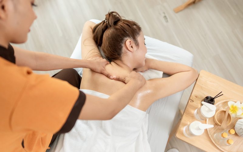 Beautiful woman getting back massage treatment with oil at beauty spa. Attractive young girl lying down on massage bed getting relaxing physiotherapy service from masseuse for body in spa clinic.
